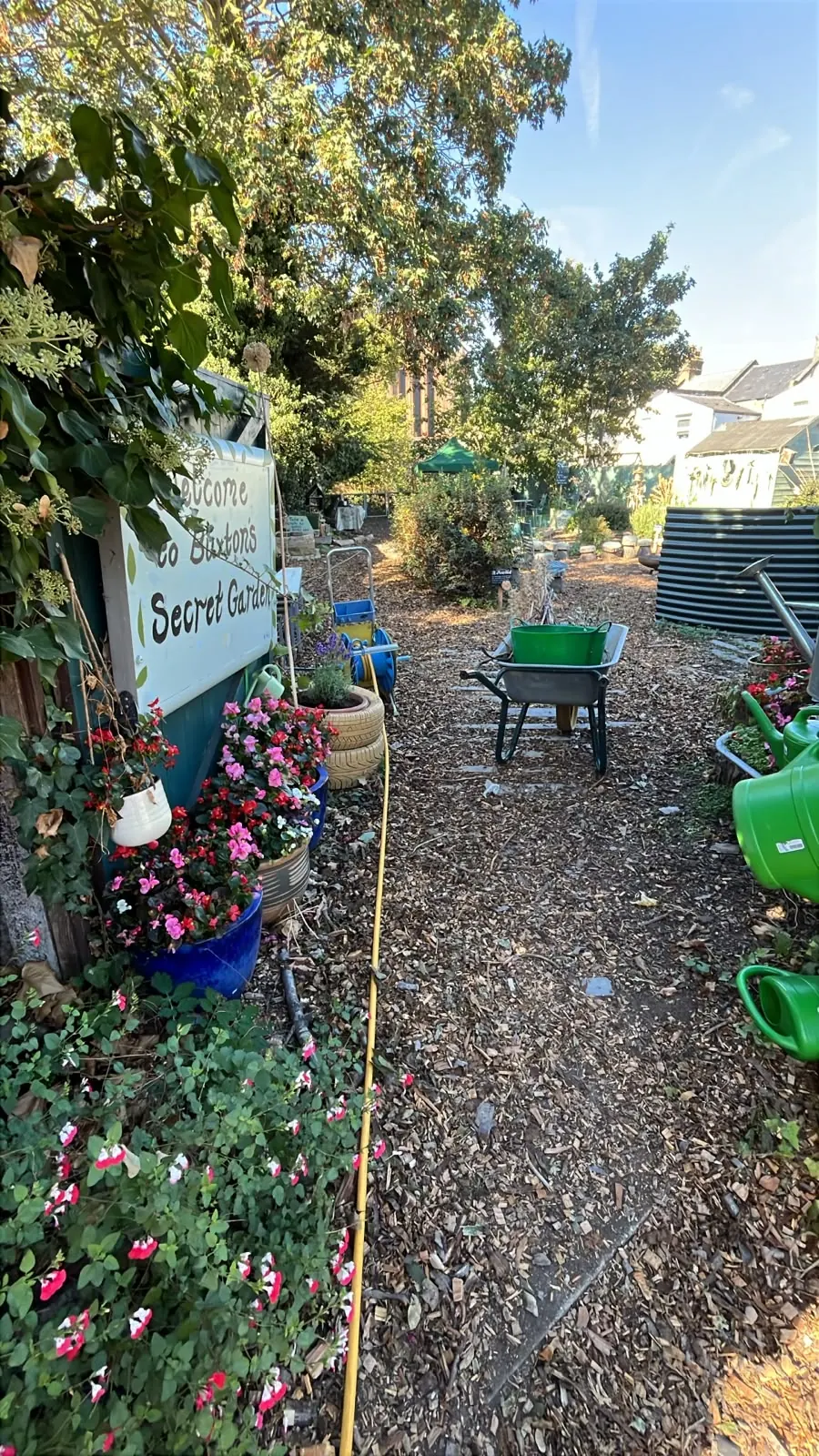 The entrance path in October, with pots of flowers beside the garden's painted name board