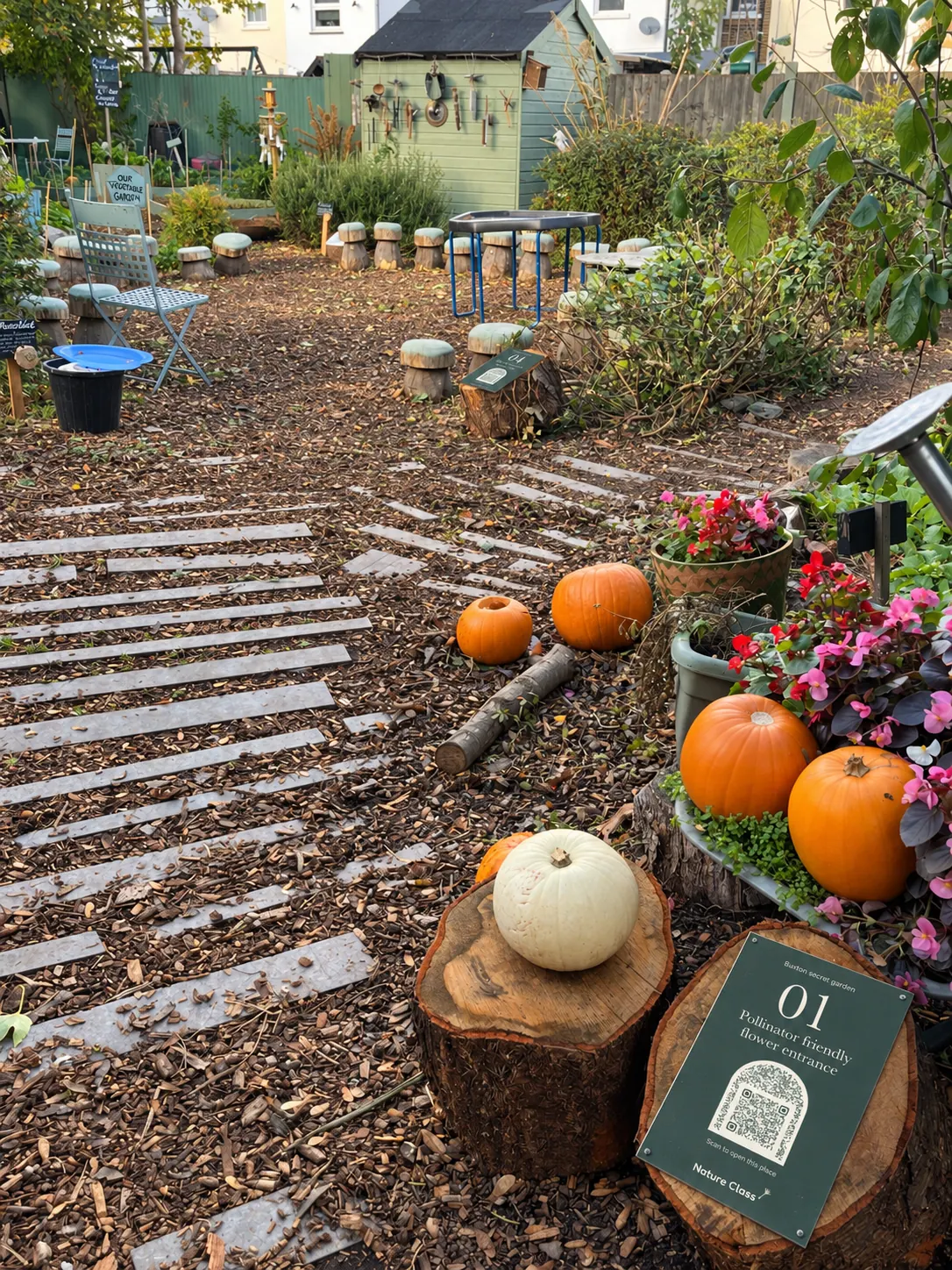 Sign 01 on a log round beside pumpkins and pots of flowers, with the stepping-stone path leading into the garden