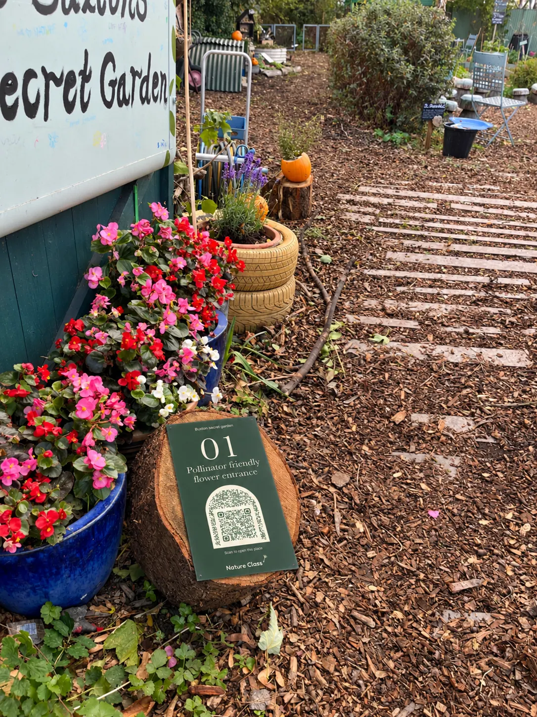 Numbered sign 01 on a log round beside blue glazed pots of begonias at the garden entrance