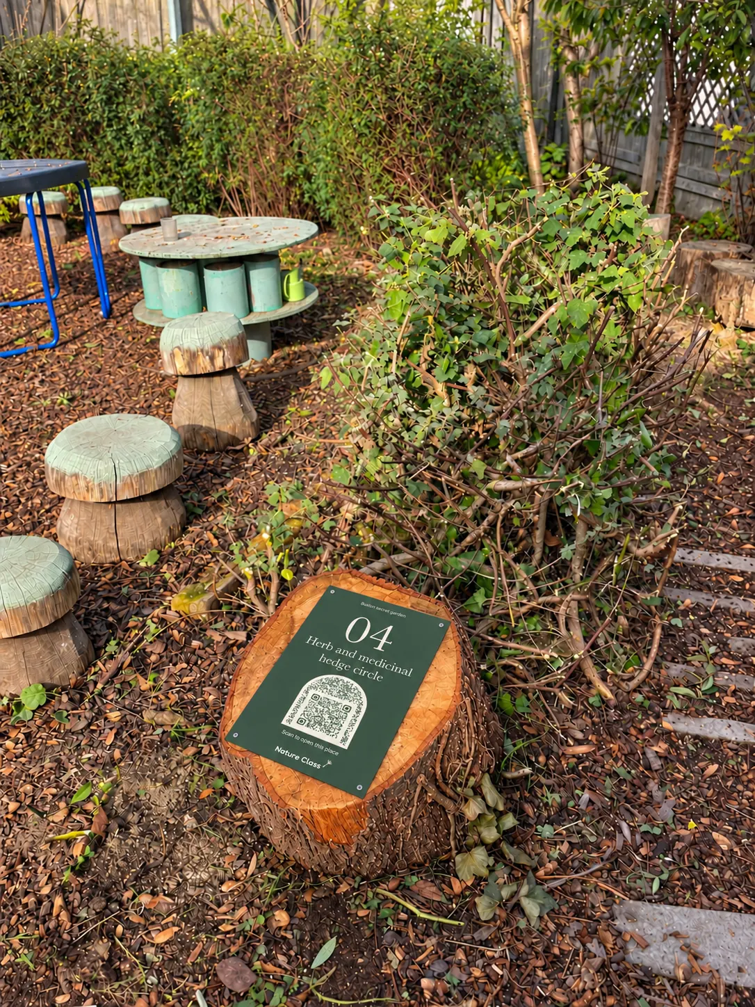 Numbered sign 04 on a log round by the herb bed, the green tool shed behind