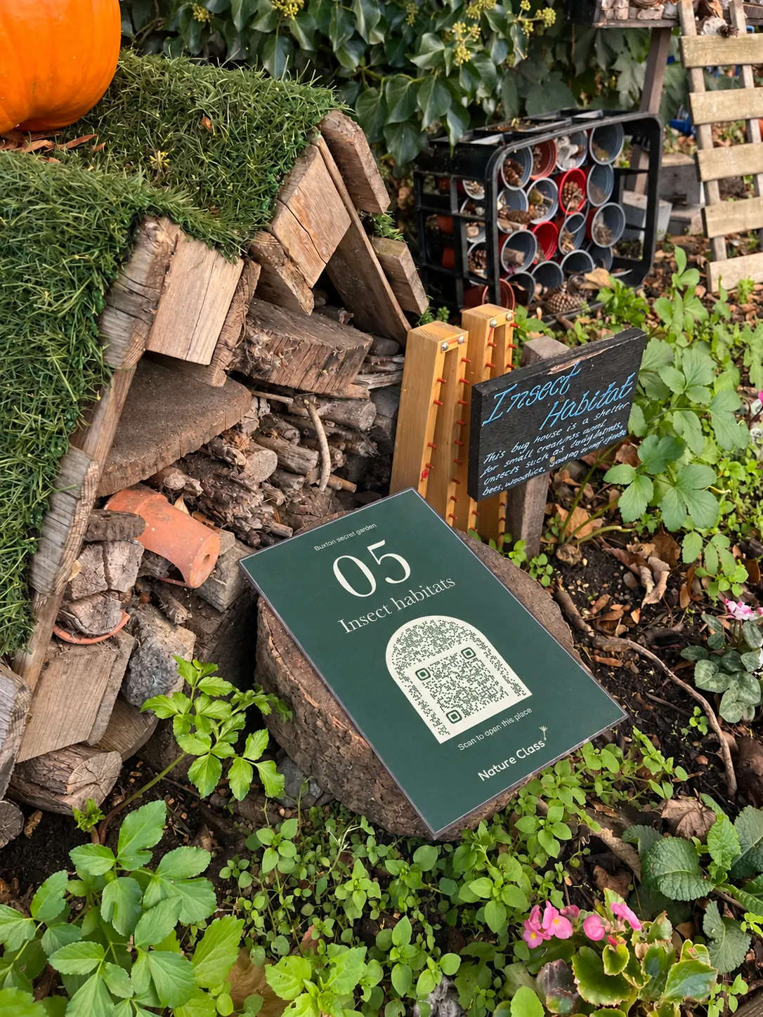 Sign 05 leaning on a log in front of the turf-roofed bug house