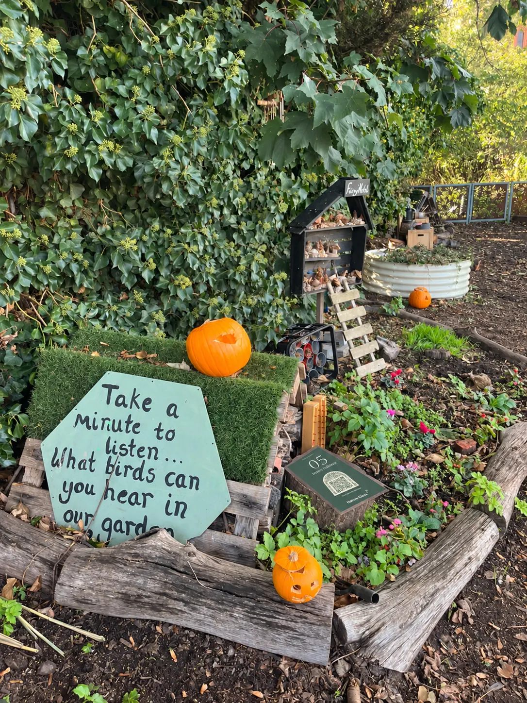 A painted board asking what birds you can hear, in front of the bug house and two pumpkins